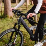 Eonic One Adventure kaufen: Dunkelgraues E-Mountainbike mit Federgabel im echten Offroad-Einsatz auf moosigem Waldboden mit Fahrer.