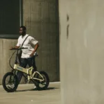 MATE FUSION kaufen: Stylisches Elektrofahrrad in Cremeweiß im realen Alltagseinsatz inmitten moderner Betonarchitektur.