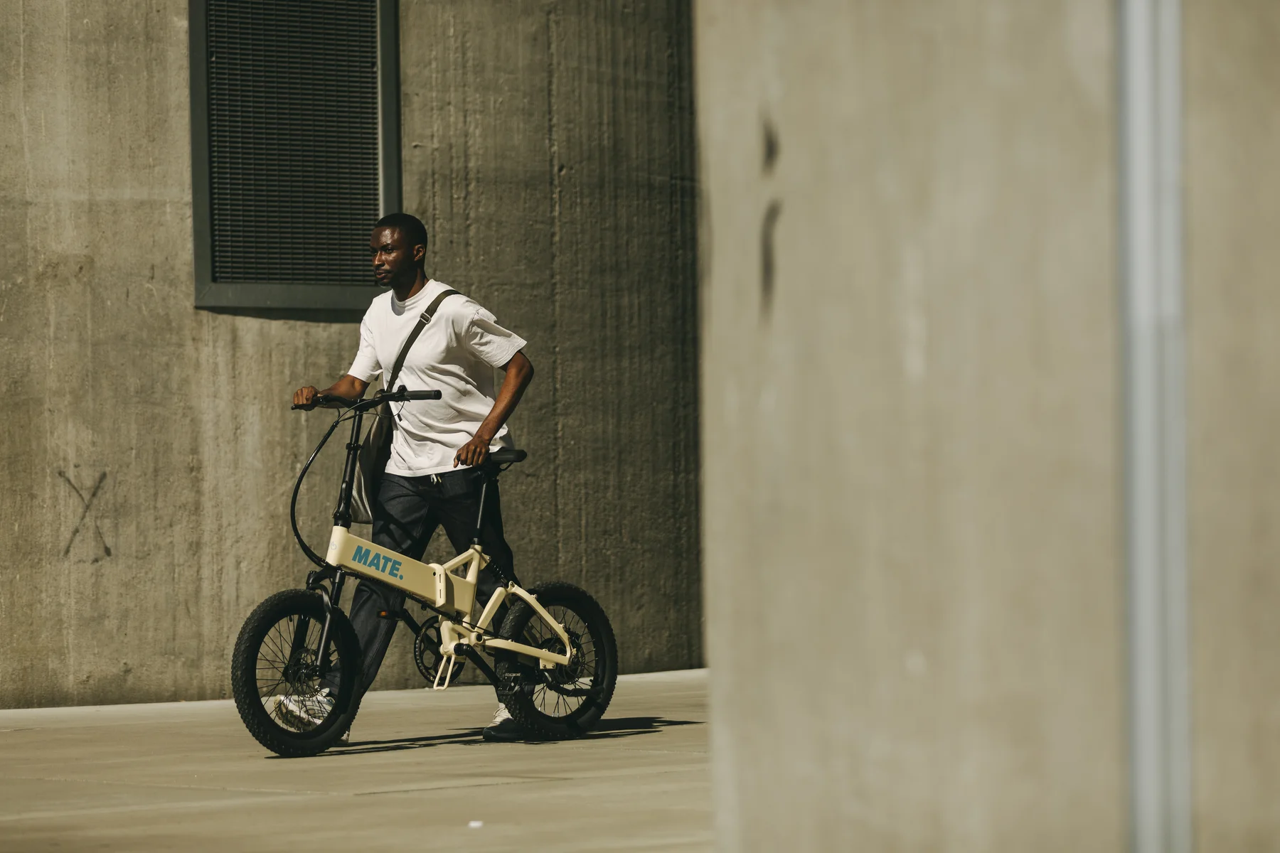 MATE FUSION kaufen: Stylisches Elektrofahrrad in Cremeweiß im realen Alltagseinsatz inmitten moderner Betonarchitektur.