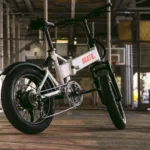 MATE X EVO kaufen: Silber-weißes Fatbike E-Bike aus tiefer Perspektive unter einer urbanen Brückenkonstruktion mit Industrieflair.
