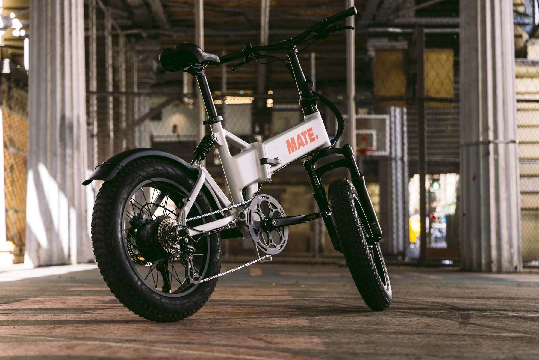 MATE X EVO kaufen: Silber-weißes Fatbike E-Bike aus tiefer Perspektive unter einer urbanen Brückenkonstruktion mit Industrieflair.