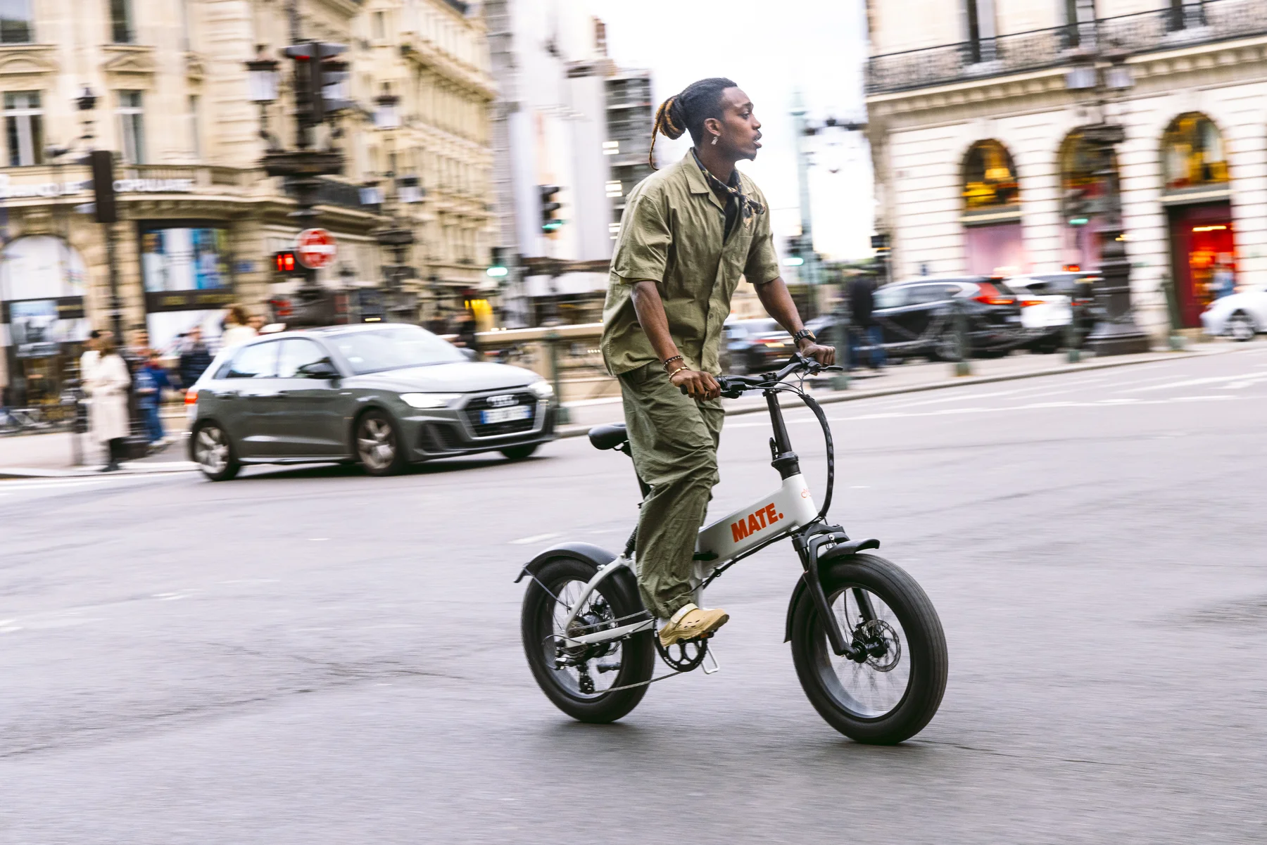 MATE X EVO kaufen: Hellgraues Fatbike E-Bike im echten Fahrbetrieb mit einem stylischen Fahrer auf einer belebten Großstadt-Kreuzung.