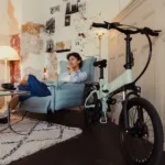 MATE ICON kaufen: Mintgrünes Faltrad E-Bike angelehnt an eine weiße Kassettentür in einer stilvoll eingerichteten Altbau-Wohnung mit einem Mann im Sessel.