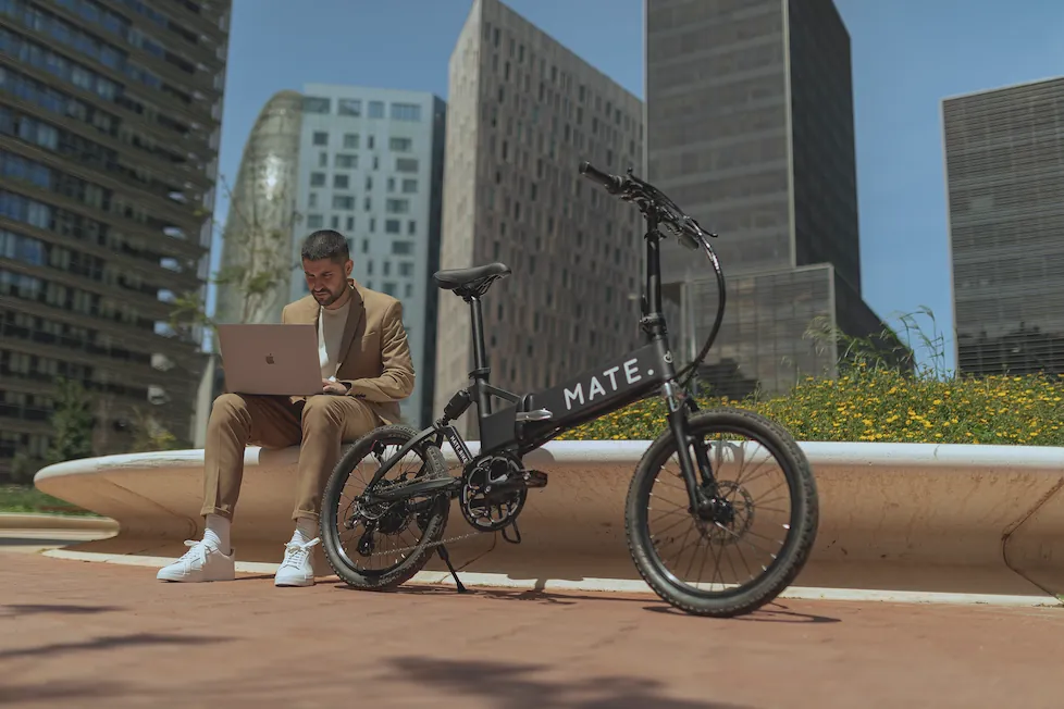 Mann sitzt im modernen Stadtumfeld mit Laptop neben einem schwarzen E-Bike – ideal für flexibles E-Bike-Leasing im Berufsalltag.