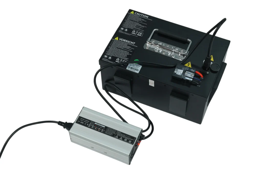 Elektroroller laden: Ein silbernes Aluminium-Ladegerät ist direkt an die entnommene, große Lithium-Ionen-Batteriebox angeschlossen.