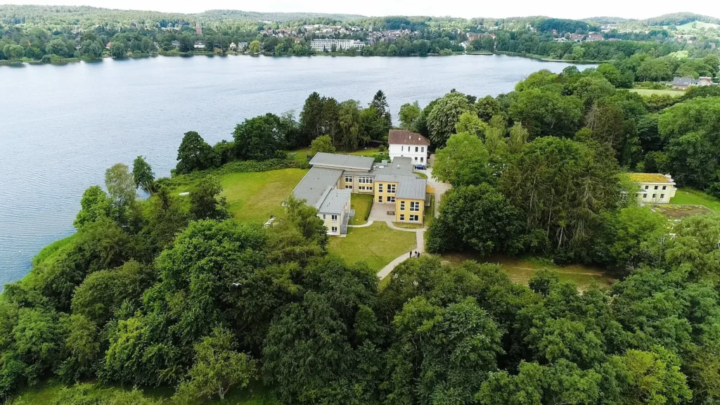 E-Bikes kaufen in Malente – Drohnenaufnahme einer grünen Halbinsel am Dieksee mit hellen Gebäuden mitten in der holsteinischen Seenlandschaft.