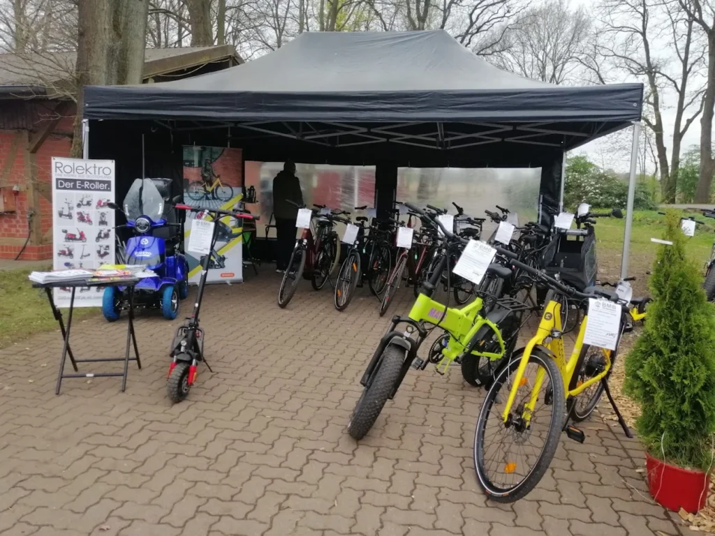 E-Bikes kaufen in Kakenstorf – BMB Ulf Baumann: Ein überdachter Outdoor-Ausstellungsstand mit zahlreichen E-Bikes, Rollern und Flyern vor dem Fahrradladen.