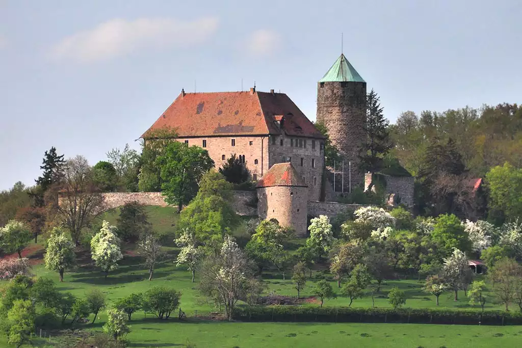 E-Bikes kaufen in Colmberg: Die historische Burg Colmberg thront auf einem grünen Hügel mit blühenden Bäumen im Frühling.